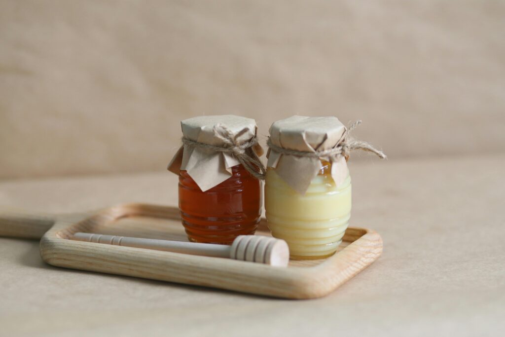 Two jars of honey on a wooden tray with a honey dipper, perfect for gourmet food styling.
